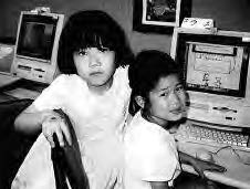 two young girls sit in front of an old style computer