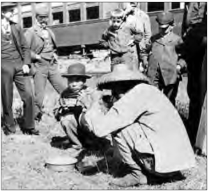 two men squat and eat while young boys watch them