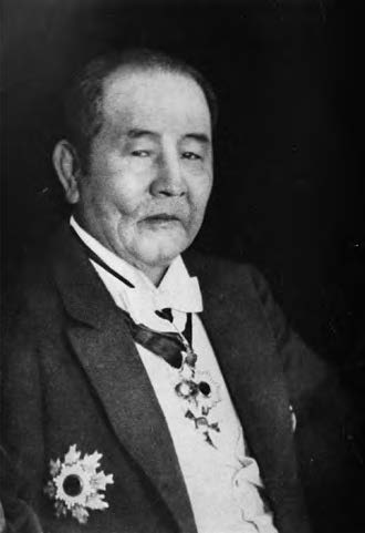 A elderly Japanese man smiles at the camera. He is wearing a Western style business suit with military badges. 