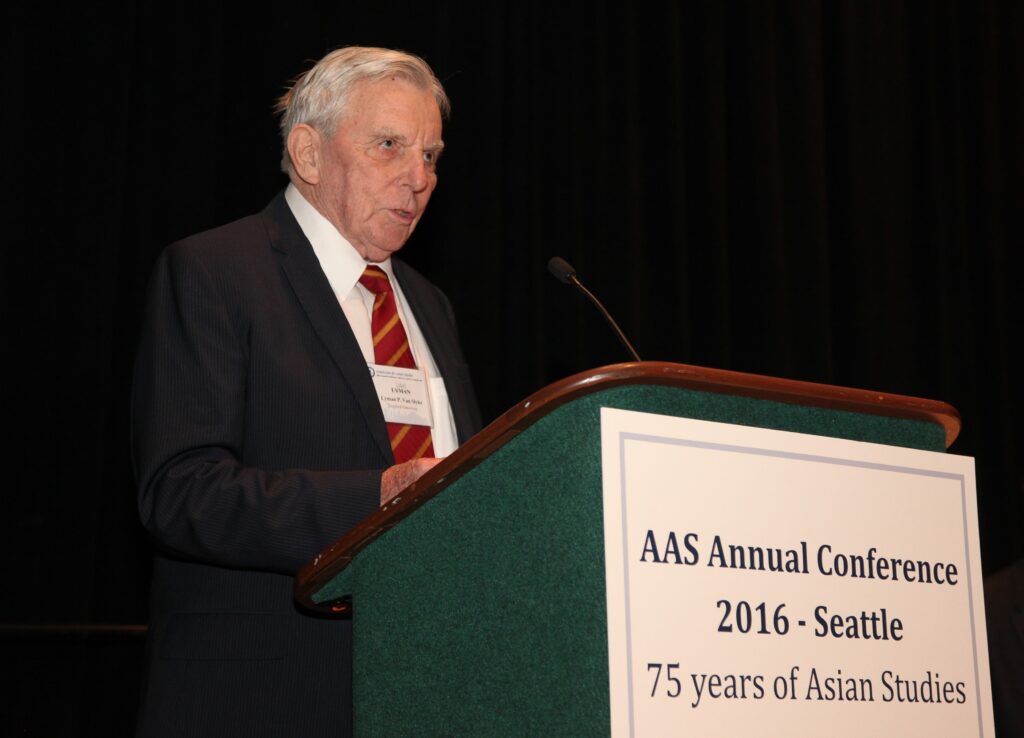 Photo of Lyman P. Van Slyke standing at a podium against a black wall.