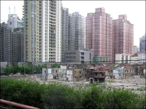 in the distance is a large skyline with close together tall buildings. in the foreground is a fenced-off area with small buildings more far apart. they look old and dilapidated.