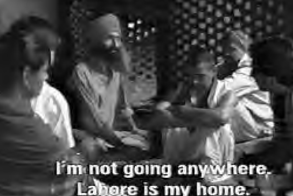 several people sitting together. the screen caption reads "I'm not going anywhere, Lahore is my home."