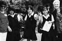 a group of school girls stand with two older women, smiling and putting up peace signs