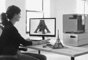 photo of a woman sitting at a computer 3D printing an Eiffel tower