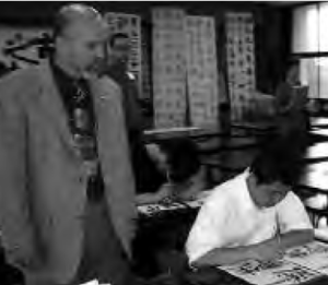 a man peers over the shoulder of a young boy as he practices his calligraphy