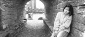 a girl sits and leans against a wall of a tunnel, looking upset