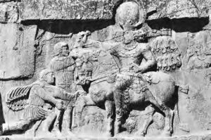 carvings into rock of a man on a horse in front of three men, one kneeling