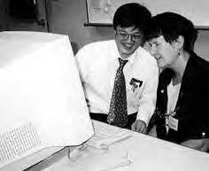 two smiling people sit and look at a computer screen 