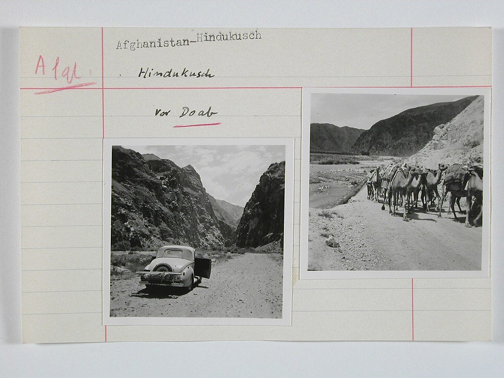 Photos from Afghanistan, 1939 or 1940. One shows an automobile sitting on a dirt road between hills. The second picture shows camels in the same scene.