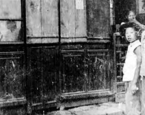 Image shows a boy standing front of closed opium den