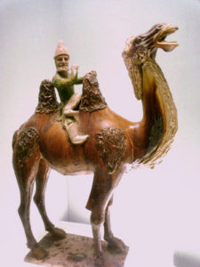 A Tang Dynasty Chinese ceramic statuette of a Sogdian merchant riding on a Bactrian camel.