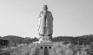 photograph of a large statue of a robed bearded man with his hands holding the middle of his chest in a sincere manner.