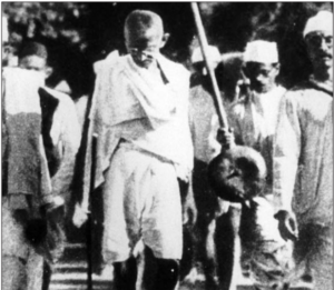 Image shows Gandhi walks in a salt march with some people following behind him