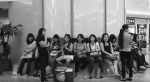 A group of female domestic workers sit and stand on a plaza bench. Domestic workers get one Sunday a month off, and Lucky Plaza is a favorite place to gather. 