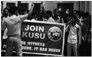 Photo shows many students raising their hands and holding the slogan reads: Be Witness—It Is Not Done, It has Begun.