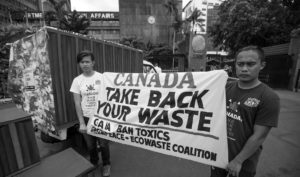 Two environmental activists hold a banner calling for the Canadian Government to take back fifty containers of mixed waste illegally shipped into the Philippines.