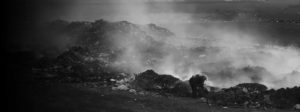 A man picks through acres of smoldering plastic, with smoke rising above him