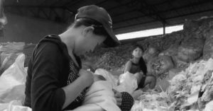 a young girl watches her mother feeds her baby, while sitting among mountains of trash