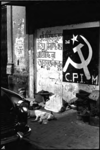 Image shows man and dog sleeping under a 1980 election-time wall poster of the CPI(M)