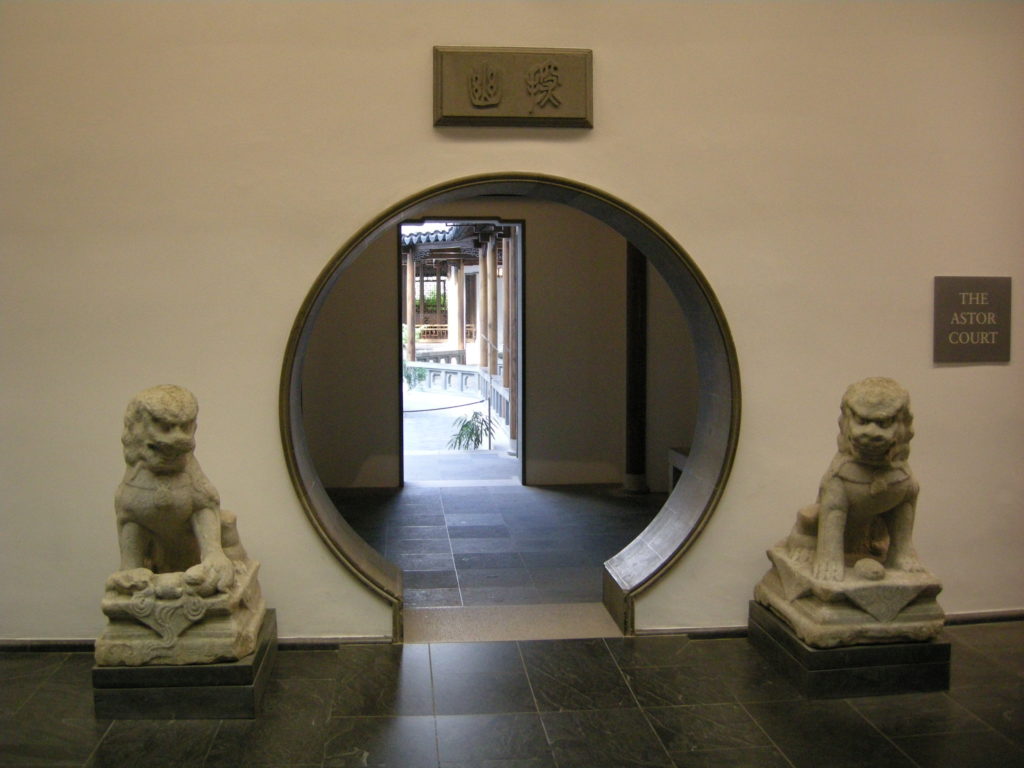 Moon door entrance to the Astor Court garden in New York’s Metropolitan Museum of Art. The door is a circular shape and is guarded by two Chinese guardian lion statues. 