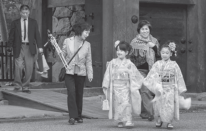 Two girls in traditional Japanese dress walking in front of the shrine with smiles on their faces, accompanied by two women.