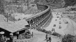 an image of rail road tracks and the wooden and metal supports underneath. workers can be seen along the tracks. 
