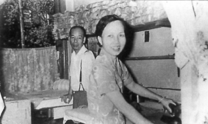 A woman in a laundry room with an iron in her hand and another man standing next to her 