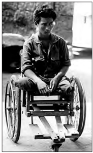 Photo of man who lost both legs sitting in wooden wheelchair