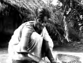 A woman squatting on the ground in front of a thatched hut