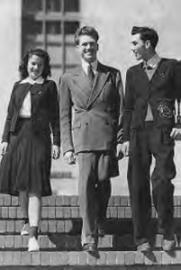 two young men in suits stand next to a young girl in a school uniform. they smile and pose for the camera
