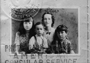A photograph of a woman and her three children. The two girls sit on either side of their mother, while the younger boy sits in the middle, in front of the mother.