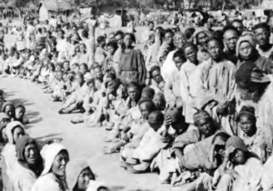 Image shows crowd of refugees sitting on the street