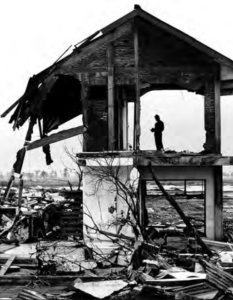 Image shows a man standing on the second floor of a destroyed home 