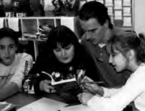 Peter Wright works with students at Brimmer and May School. Three female students are reading a book, and Peter Wright is looking at the book they are pointing. 