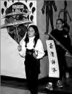 Students parade through the hallways of New Prospect Elementary School in Alpharetta, Georgia. One girl is holding a kite and other girl is holding a banner. On the banner writes four characters. 