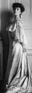 a woman in a dress poses with her chin held high and arms behind her back.
