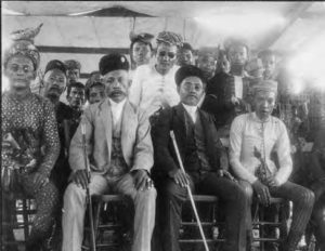 photograph of well-dressed men and women sitting, holding canes. some peek their heads out from behind the others to be seen.