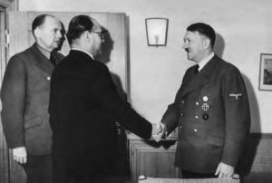 two men shake hands, while another man looks on.