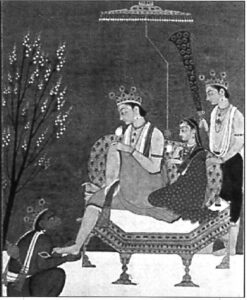 two people including one with a crown sit on a chair while another touches the crowned one's foot. 