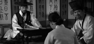 Screenshot of two men in traditional Korean dress talking seriously to a woman
