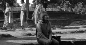 Image shows a woman sitting on the ground with three monks walking behind her