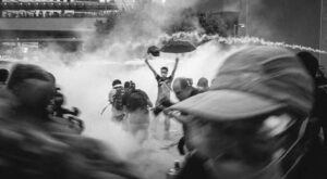 a photo of a man holding his arms above his head amidst chaos and smoke