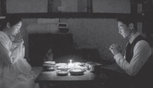 black and white photo of a man and woman praying over a candle and table of food