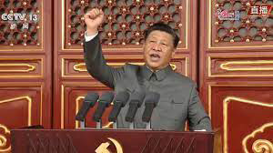 photograph of a man standing at a podium with many microphones, holding his fist in the air.