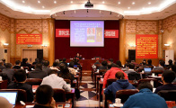 photograph of a large scren in front of rows of people in chairs as the audience.