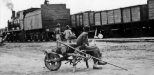 Image shows a wheelbarrow coolie watching the train. 