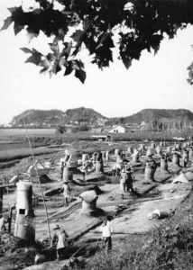 Photograph of people walking between large furnaces that protrude out of the ground.