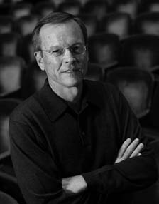 Photograph of Frank Upham smiling, a middle-aged white man with a full head of hair and with glasses. He is wearing a simple black long sleeve shirt. 