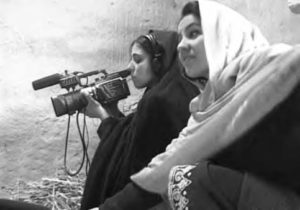 two girls with hijabs hold and look through a camera
