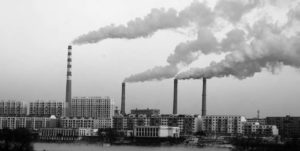 smoke stacks spilling out thick plumes of smoke rise about a city skyline